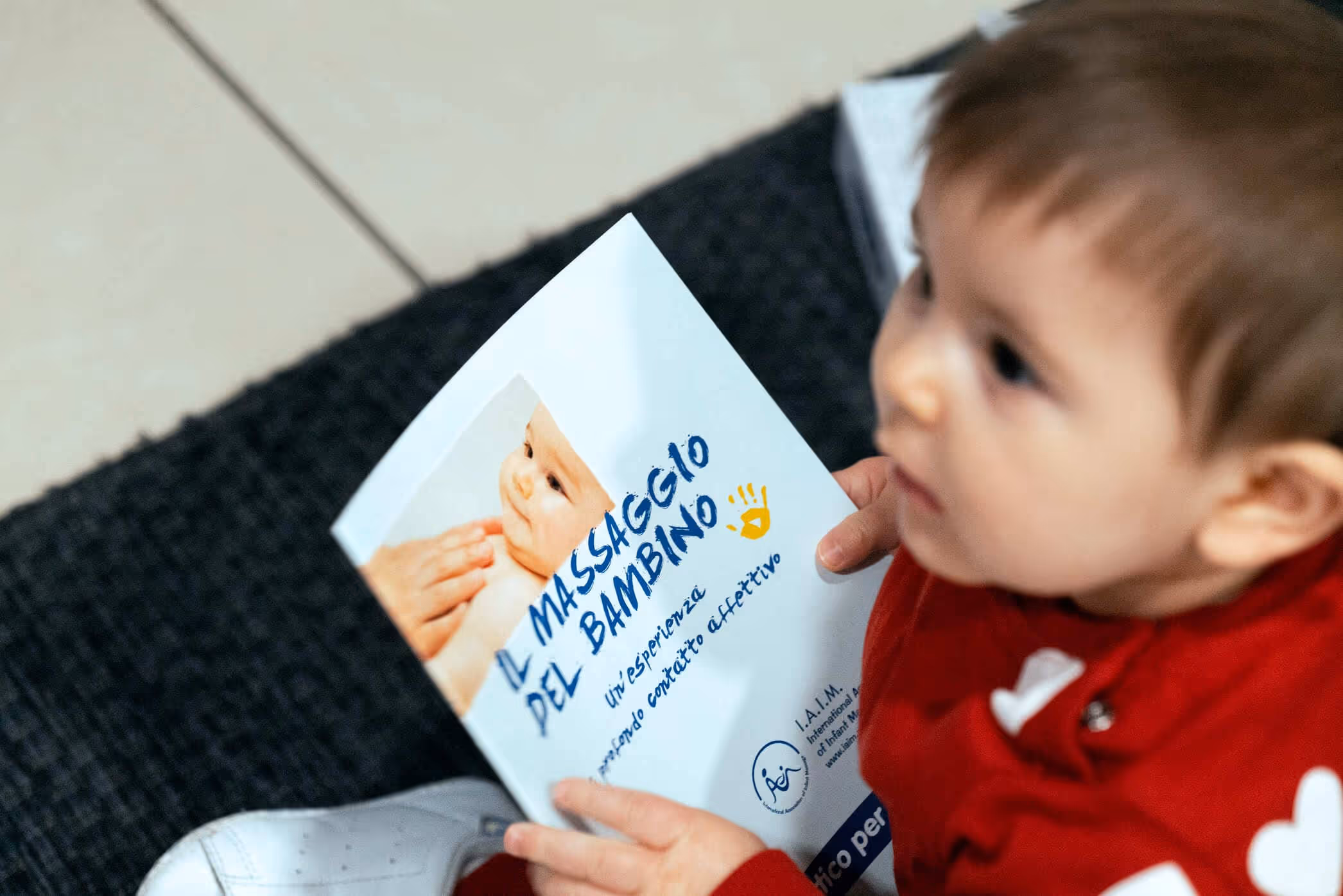 Nenonato che guarda la mamma mentre regge una locandina di massaggio infantile